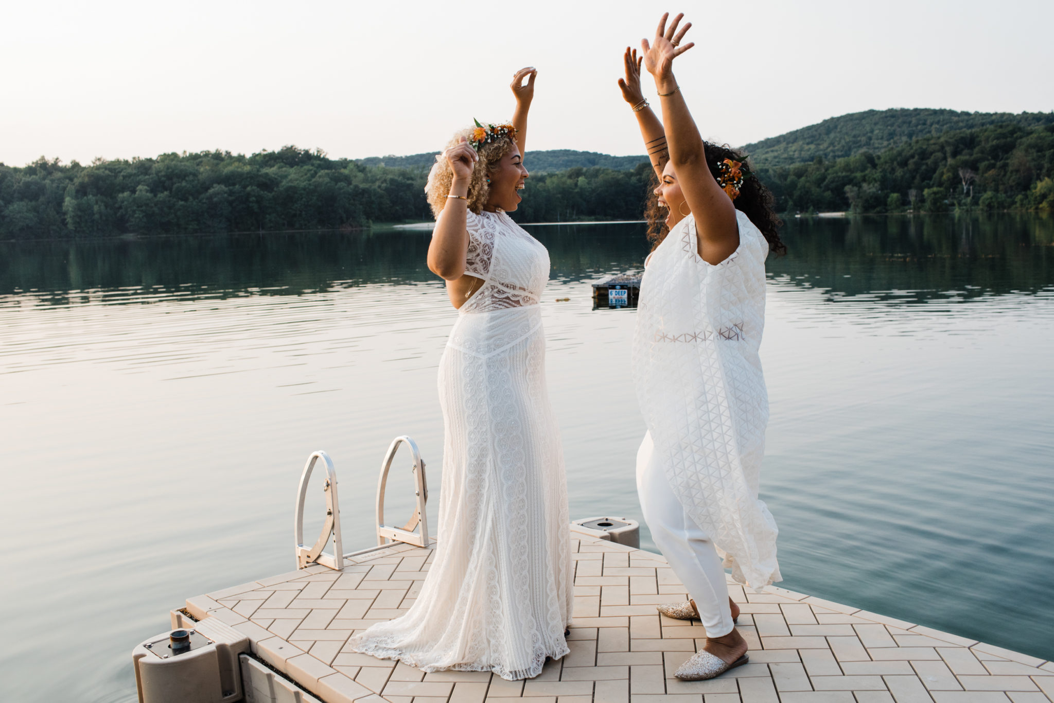 two brides standing on a dock with their hands in the air