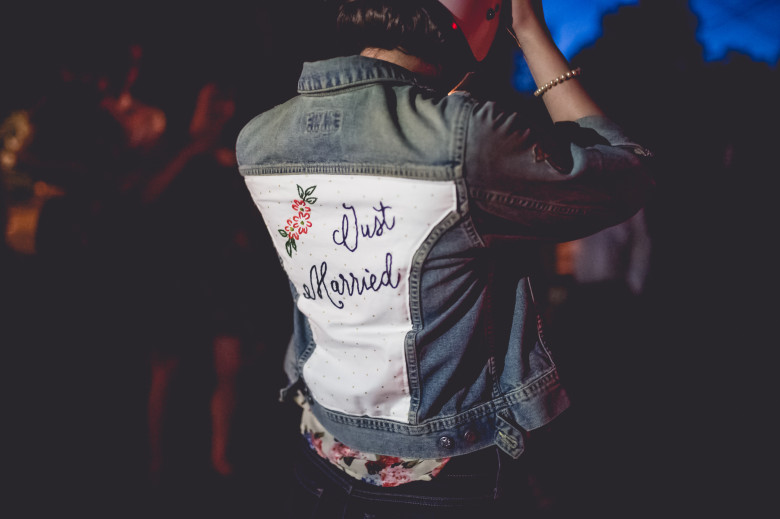 A woman puts on a motorcycle helmet while wearing a denim jacket with an embroidered back that reads "Just Married"