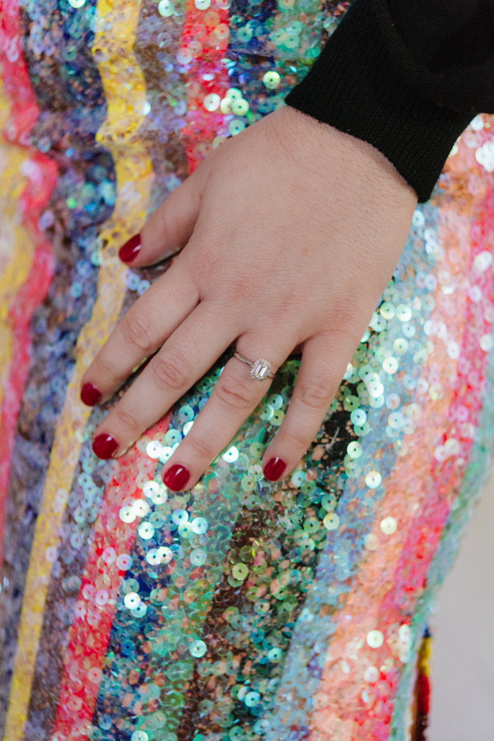 Walmart synthetic diamond engagement ring on a woman's hand resting on a rainbow sequined skirt