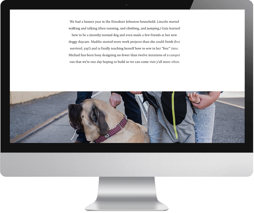 A computer monitor displaying a page from a Squarespace family website features a text paragraph enumerating family successes from the year past above an image of a man holding the leash of an English Mastiff and a woman holding the hand of a baby in a grey bat hooded onesie. 