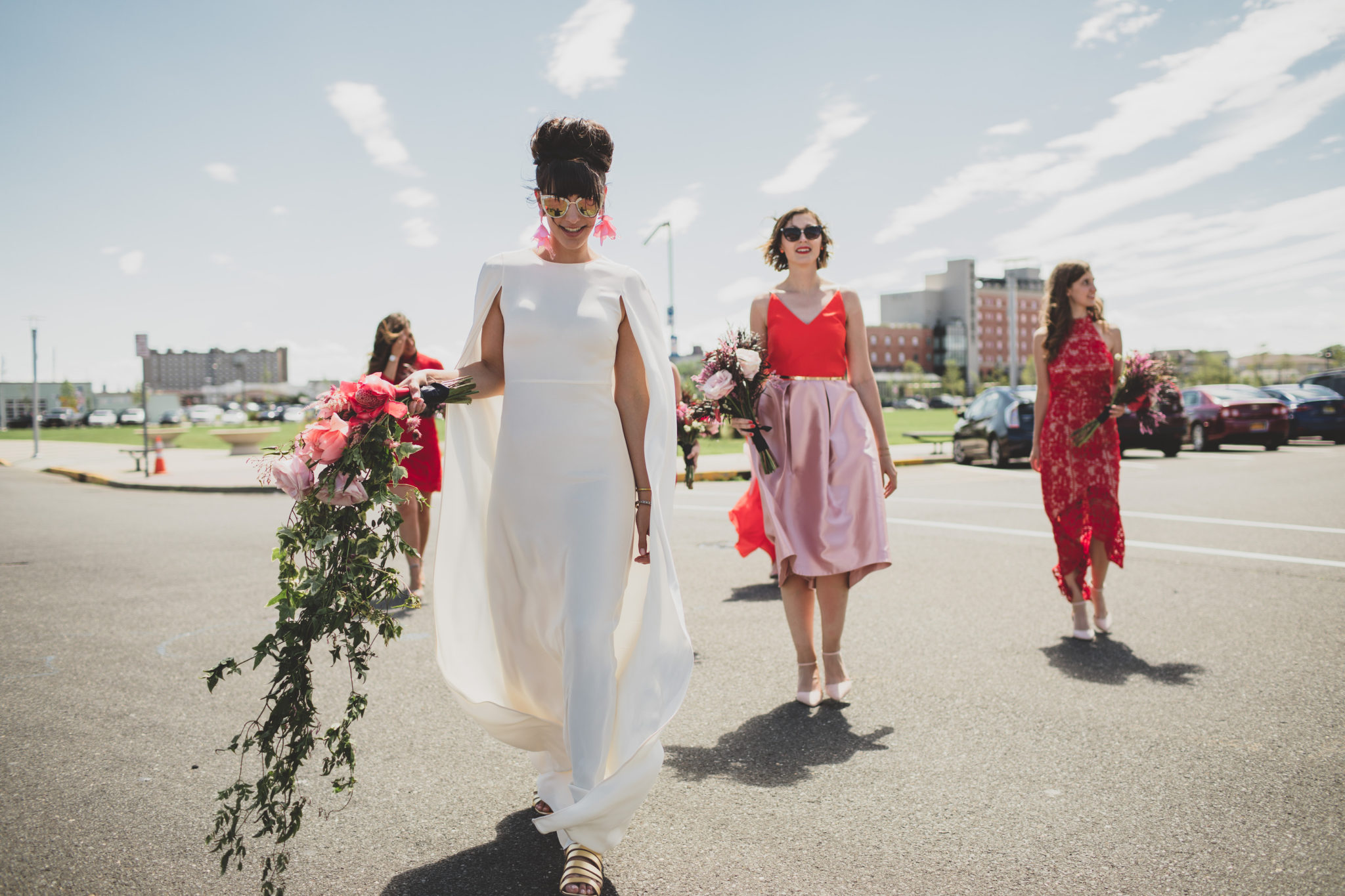 bride wearing a wedding dress with a cape and cascading bouquet with bridesmaids in mismatched hot pink and red dresses