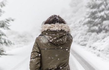 A woman in a fur trimmed parka walks away from you down a snowy lane