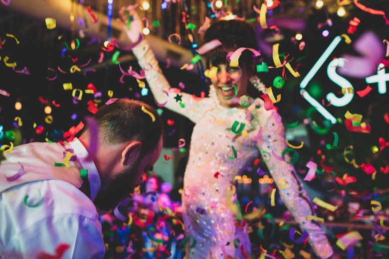 Two people on the dance floor at their wedding reception being showered with colorful ribbon confetti as they dance to the best wedding songs of 2019