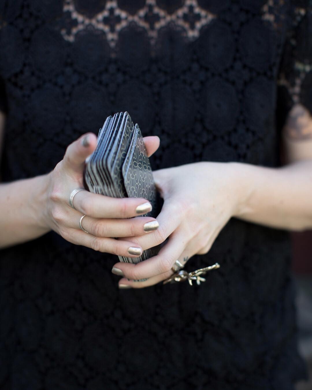 A woman in a dark lace dress with gold nails and gold rings shuffles a deck of Fleurot tarot cards for wedding tarot