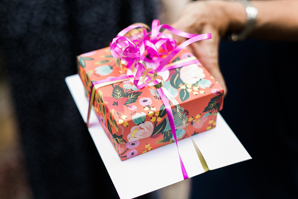 Woman holding a wedding present wrapped in Riffle Paper gift wrap and pink and gold curly ribbon at a destination wedding