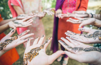 A group of women stand in a circle and extend their hands to show their mendhi