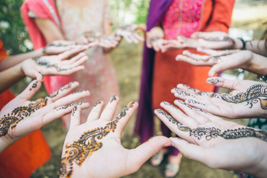 A group of women stand in a circle and extend their hands to show their mendhi