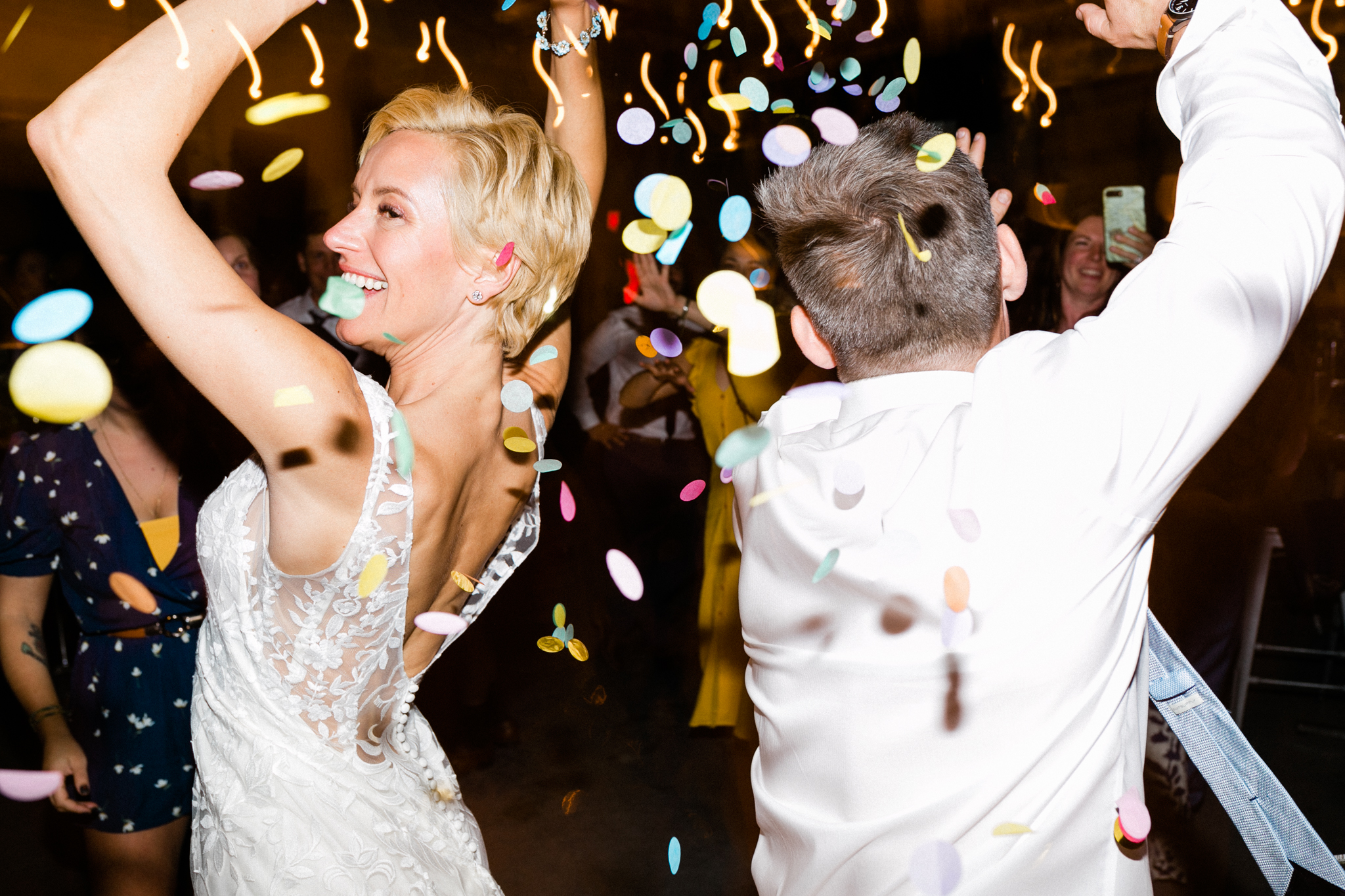 bride and groom dancing with their arms up and confetti falling all around them in a photo by Laura Ford