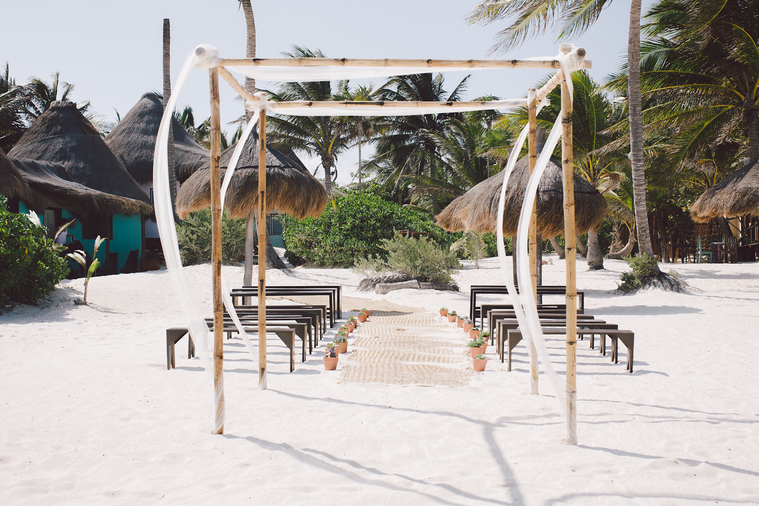 A bamboo wedding gazebo and benches and a grass mat aisle set up on a beach for a destination wedding