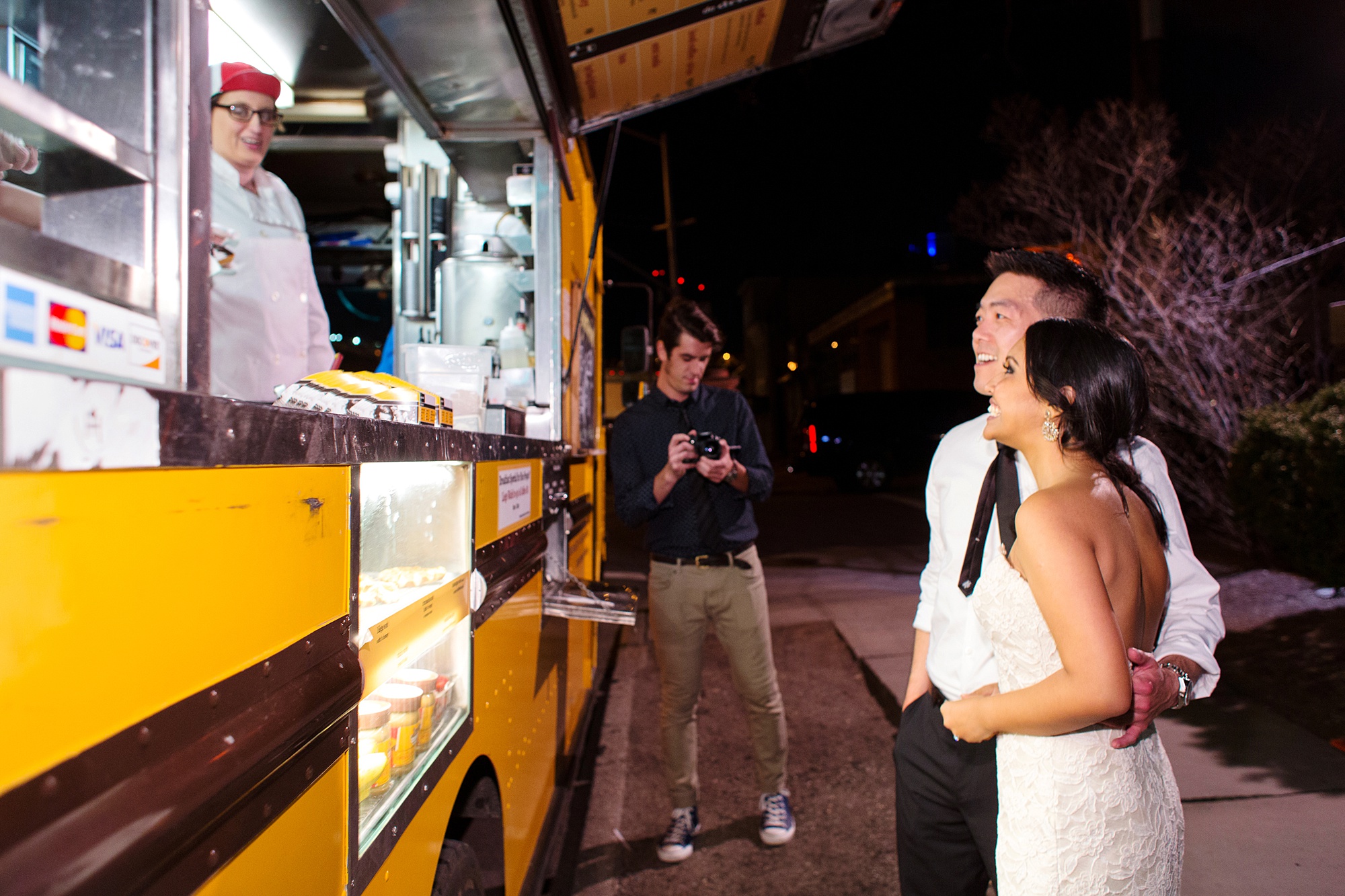 Wafels & Dinges food truck is shown from the side at night with bride and groom standing in front of window deciding what to order as cook smiles back in a photo by Kyo Morishima