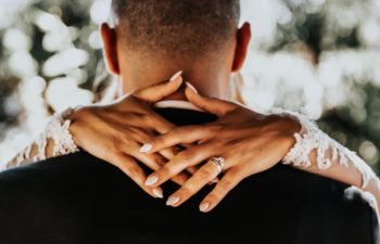 A close up of the back of a groom's shoulders and head with a bride's arms around his neck