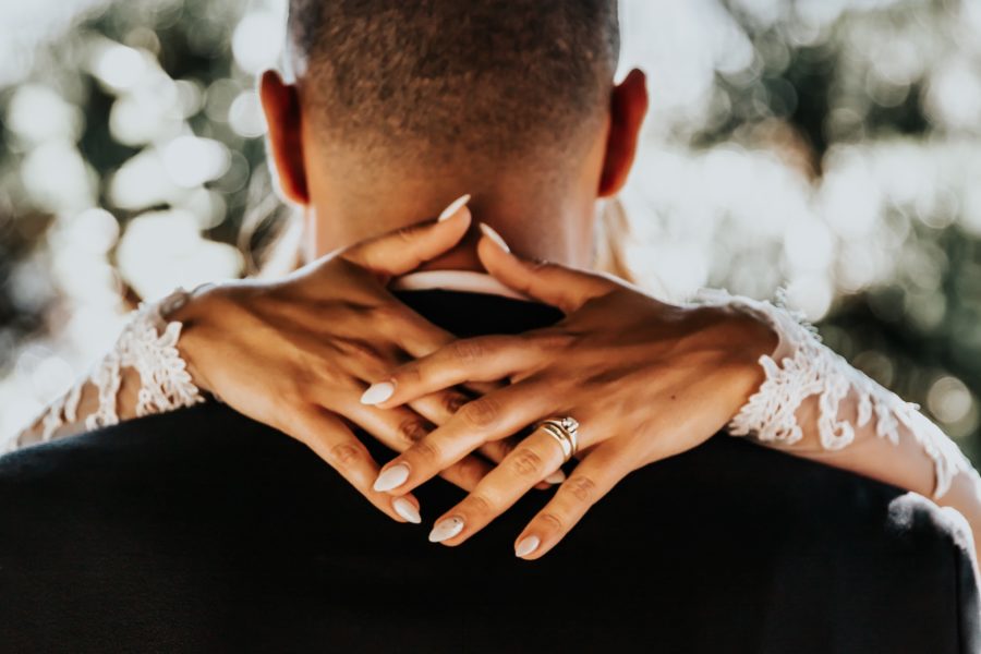 A close up of the back of a groom's shoulders and head with a bride's arms around his neck
