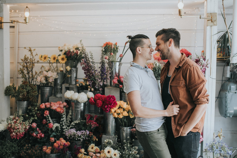 two men embrace in a flower mart for an engagement photo