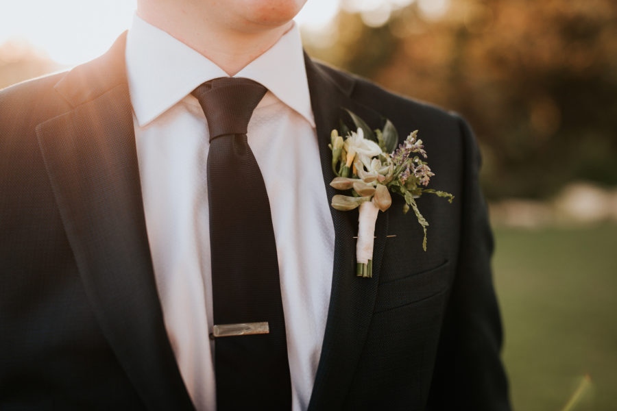 Close up portrait of the torso of a man in a dark suit with a floral boutonnière