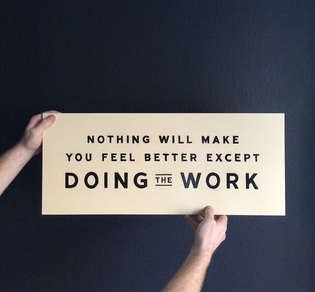 Hands hold a sign that reads "Nothing will make you feel better except doing the work"