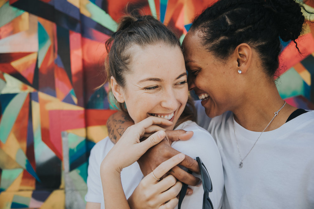 LGBTQ engagement photo in front of a brightly patterned graffitti wall