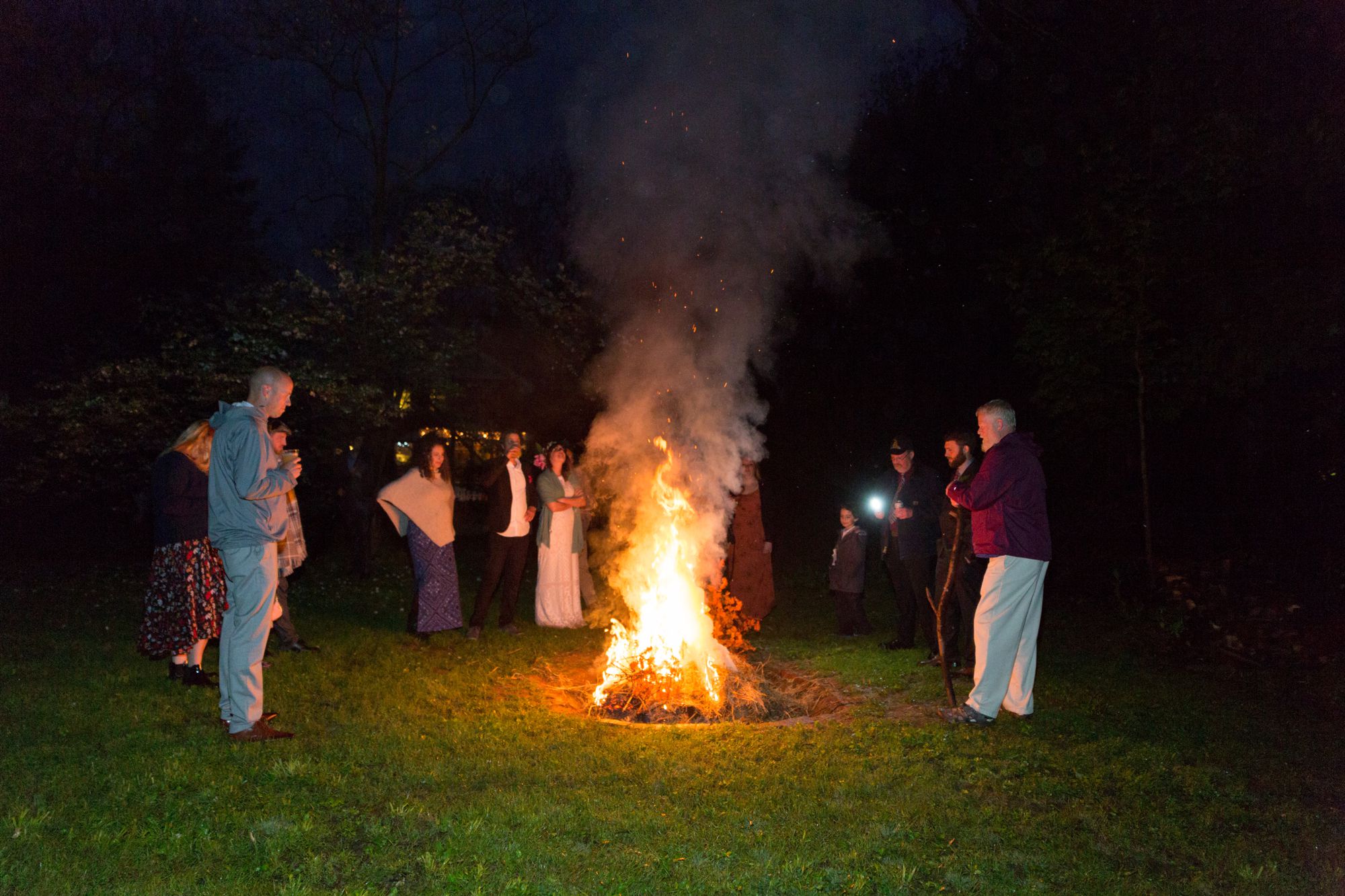 people surrounding a bonfire at a backyard wedding