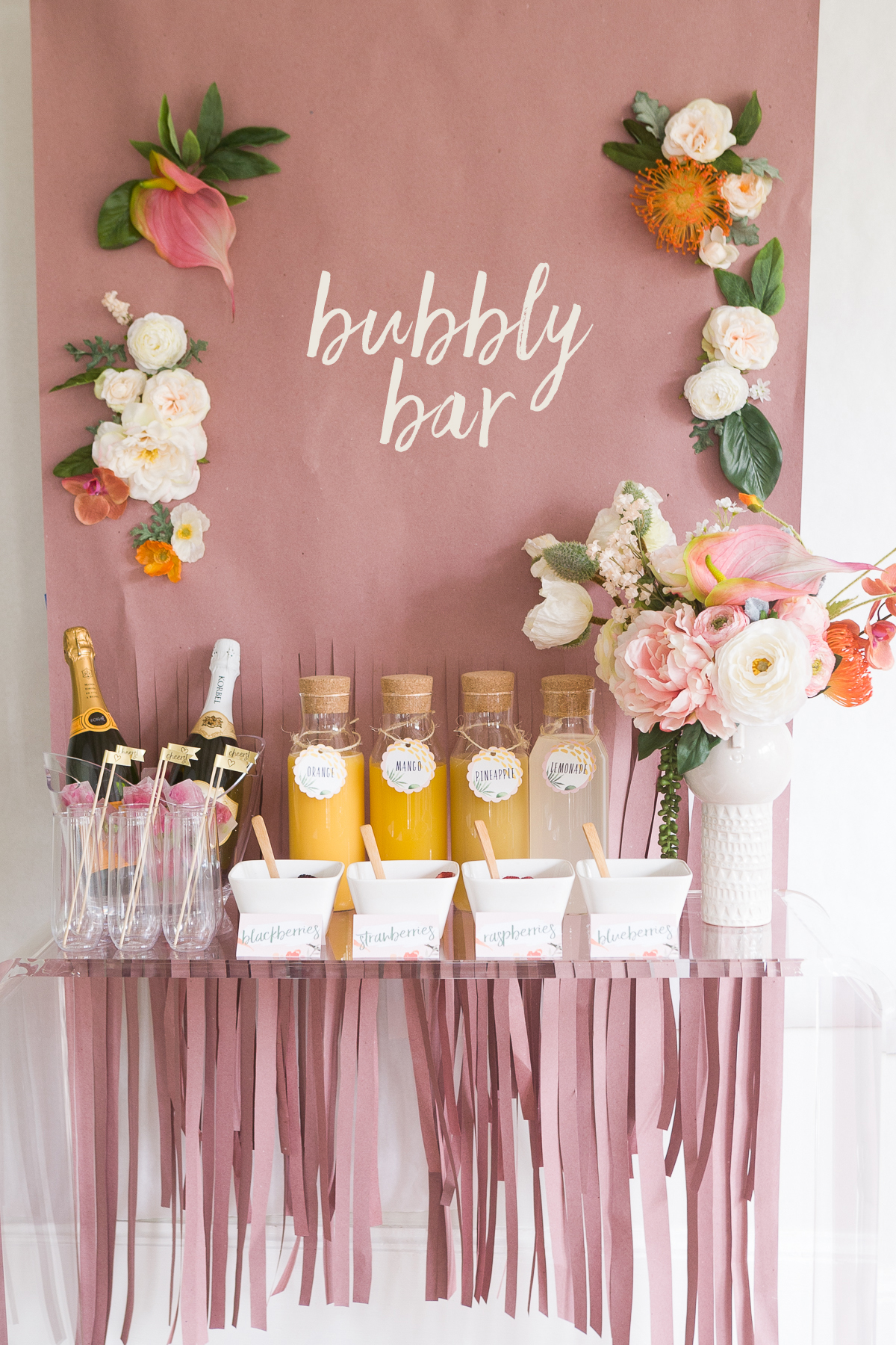 Juices and champagne on a table with a backdrop of flowers and bubbly bar sign as an idea for bridal shower decorations