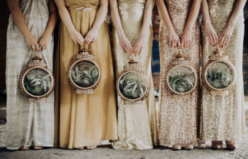 five women in shimmery metallic full-length dresses hold round copper lanterns filled with air plants for a wedding without flowers