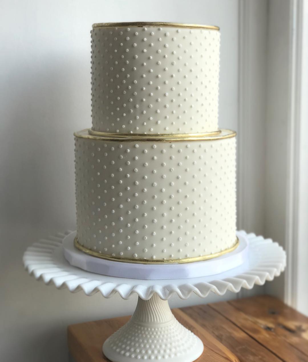 a two-tiered white wedding cake covered in frosting dots