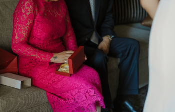 A woman in a bright pink lace dress opens a red jewelry gift box in her lap containing bracelets