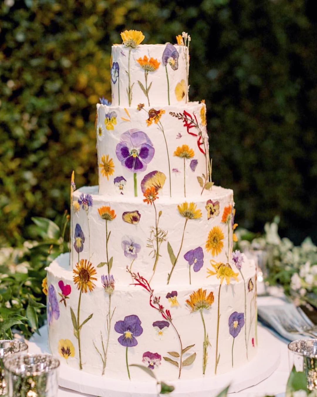 a 4 tiered white wedding cake covered in pressed flowers