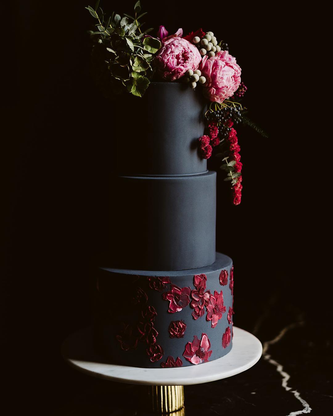 a 3-tiered black wedding cake covered in pink and red flowers