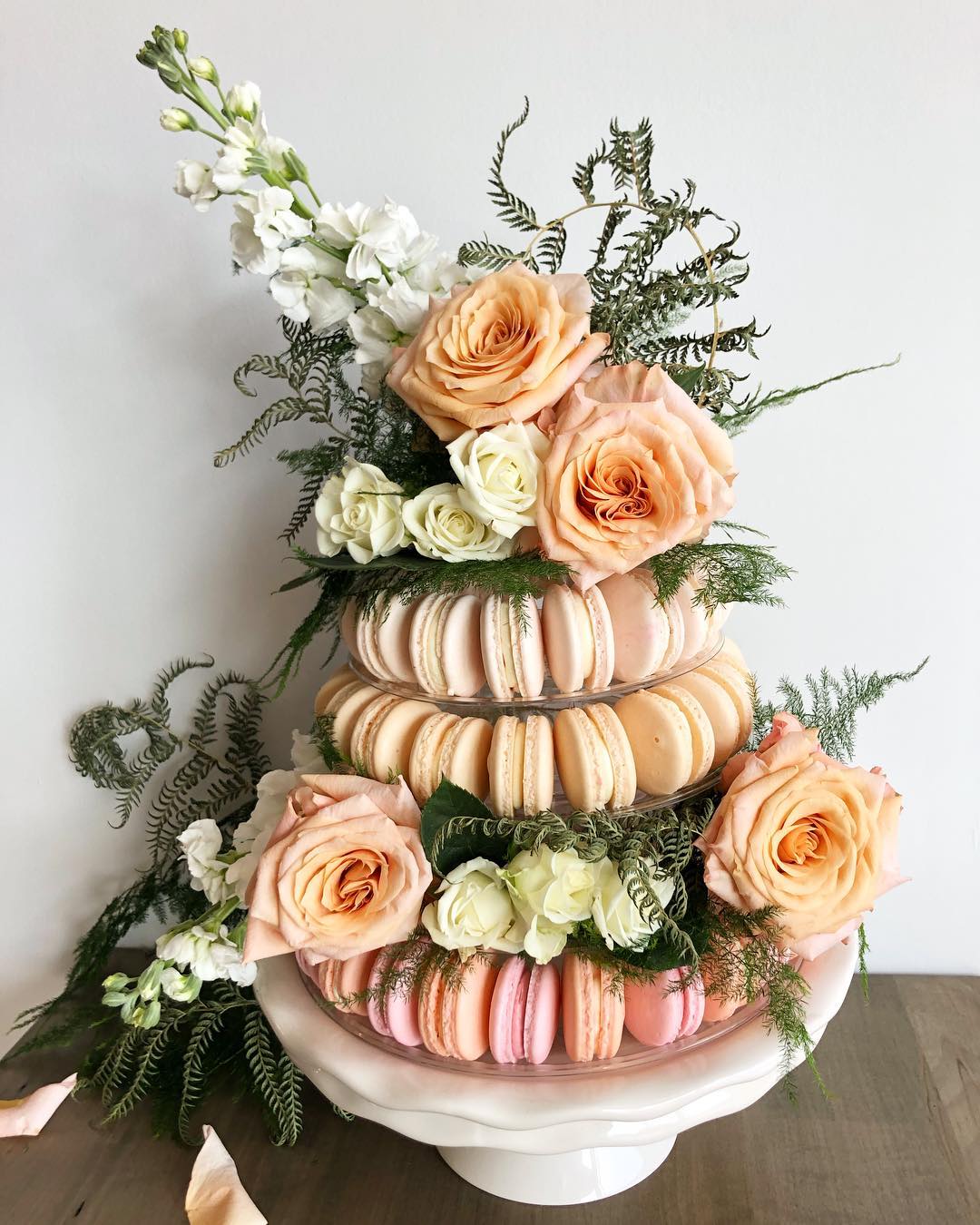 tower of pink, orange, and yellow macarons topped with roses and greenery