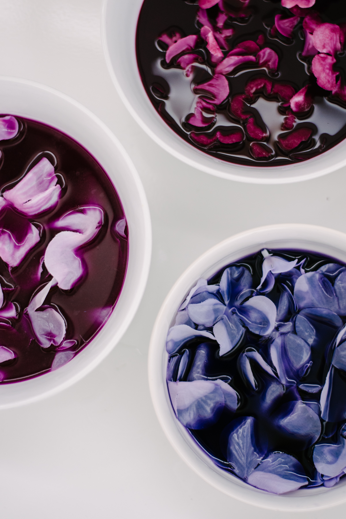 Overhead shot of white fabric flowers being immersed into bowls of Rit dye