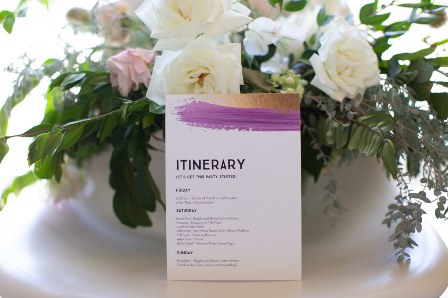 An Itinerary card leans against a pink and white flower arrangement