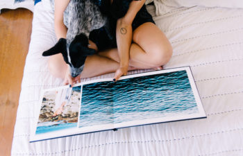 A person sits on a bed looking through a photo book while holding a black and white dog on their lap