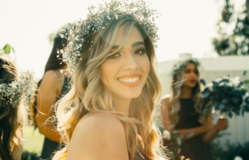 A woman in a baby's breath flower crown and hair in beachy waves smiles at you