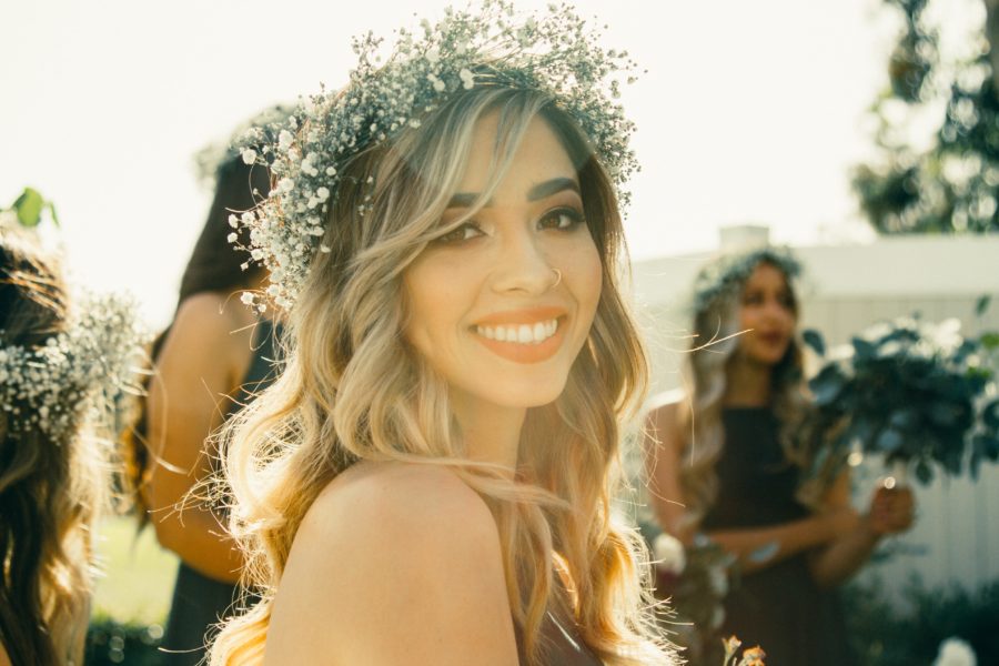 A woman in a baby's breath flower crown and hair in beachy waves smiles at you