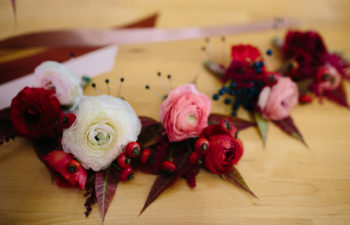 Pink, red, and white flower crowns with ribbons sit on a wooden table