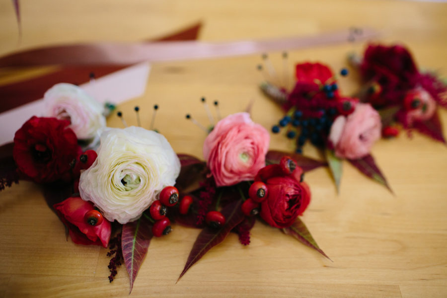 Pink, red, and white flower crowns with ribbons sit on a wooden table