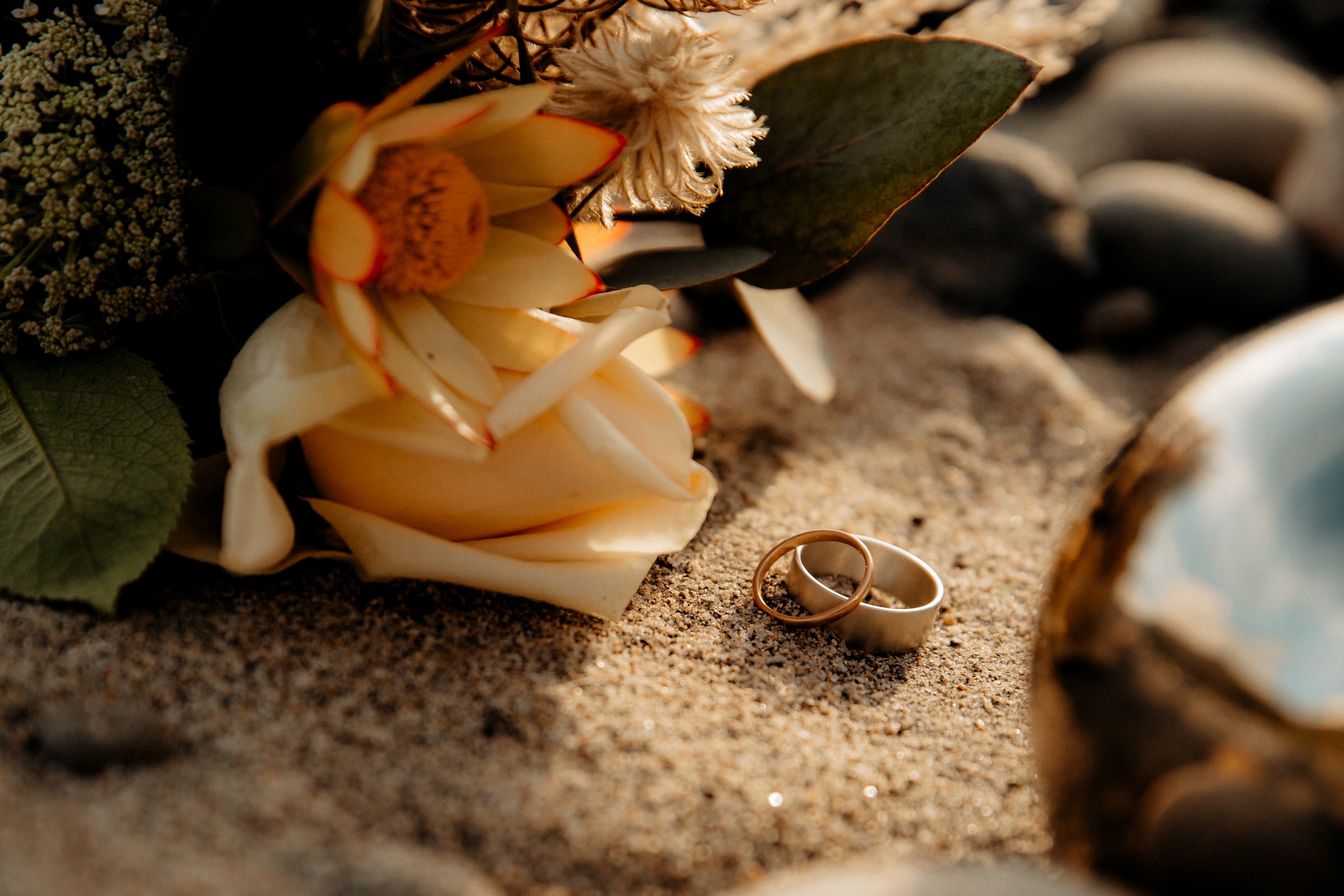 Two rings leaning against each other in the sand - Good Gold