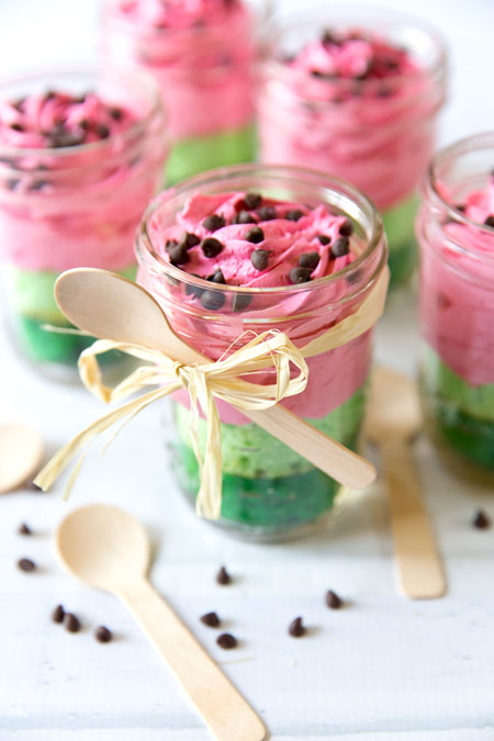 Cakes in mason jars dyed to look like watermelons, with spoons tied with twine for bridal shower favors