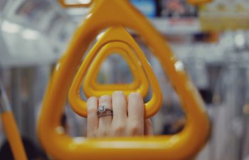 A womxn's hand with an engagement ring holds onto a triangle-shaped yellow handle on public transit