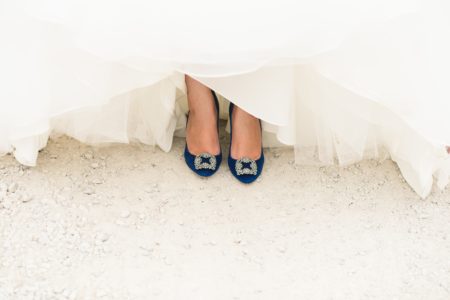 A womxn's black pointed toe heels with rhinestone accents poke out from under her voluminous wedding dress