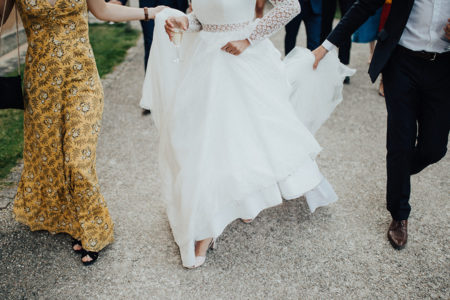 A bride in a white wedding dress walks down the street with helpers