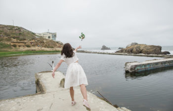 A woman throws her flower bouquet into the ocean
