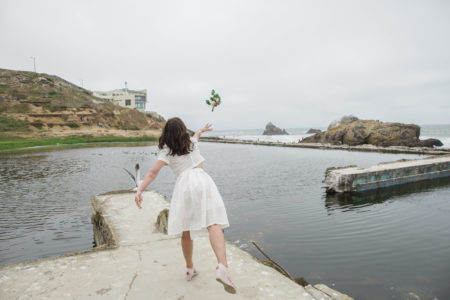 A woman throws her flower bouquet into the ocean