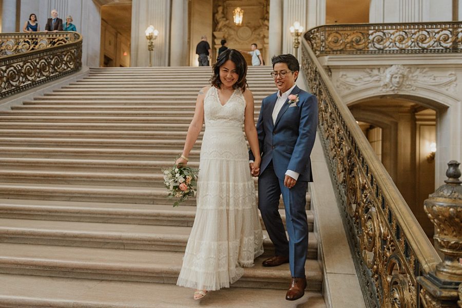 A wedding couple walk down steps at the San Francisco City Hall
