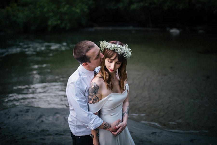 A wedding couple embrace while standing in a river
