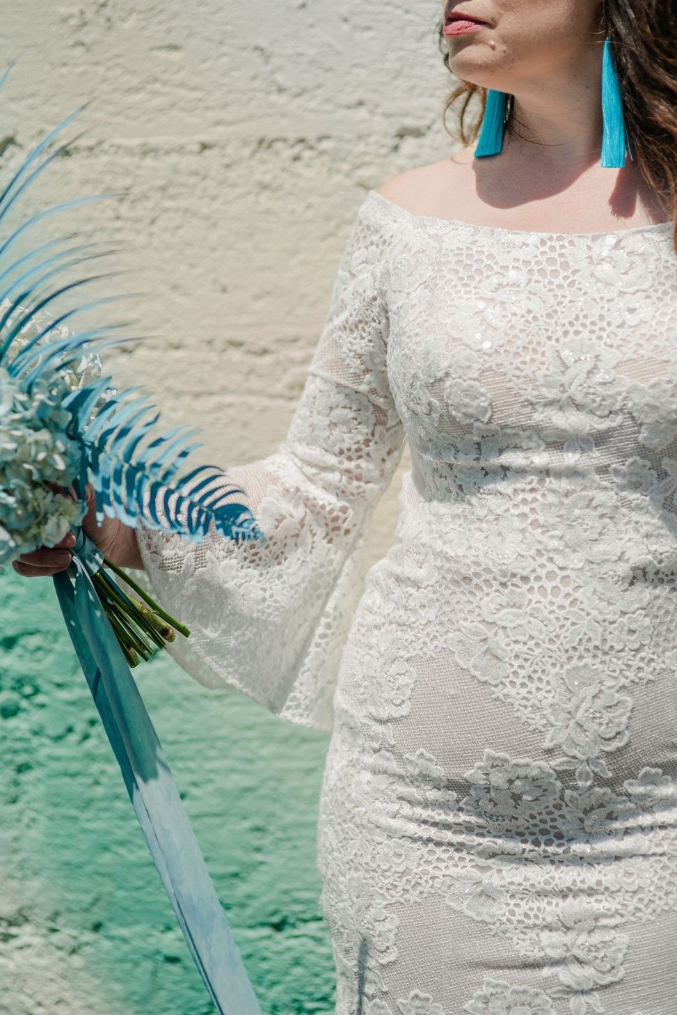 closeup of a woman wearing a long sleeve lace gown from madison james holding a blue bouquet and wearing blue fringe earrings