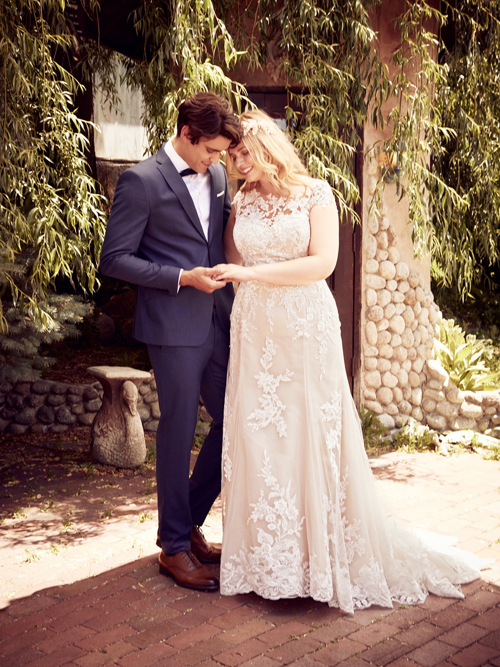 a couple embraces in front of a building covered in vines. The bride is wearing the liesl lynette gown by Rebecca Ingram