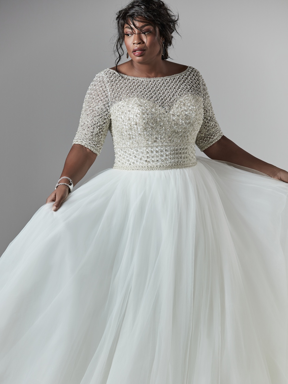 a black bride poses wearing the darren lynette long sleeve beaded plus size wedding gown by sottero and midgley