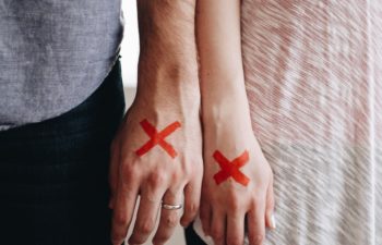 a couple stand side by side with red X's on their hands