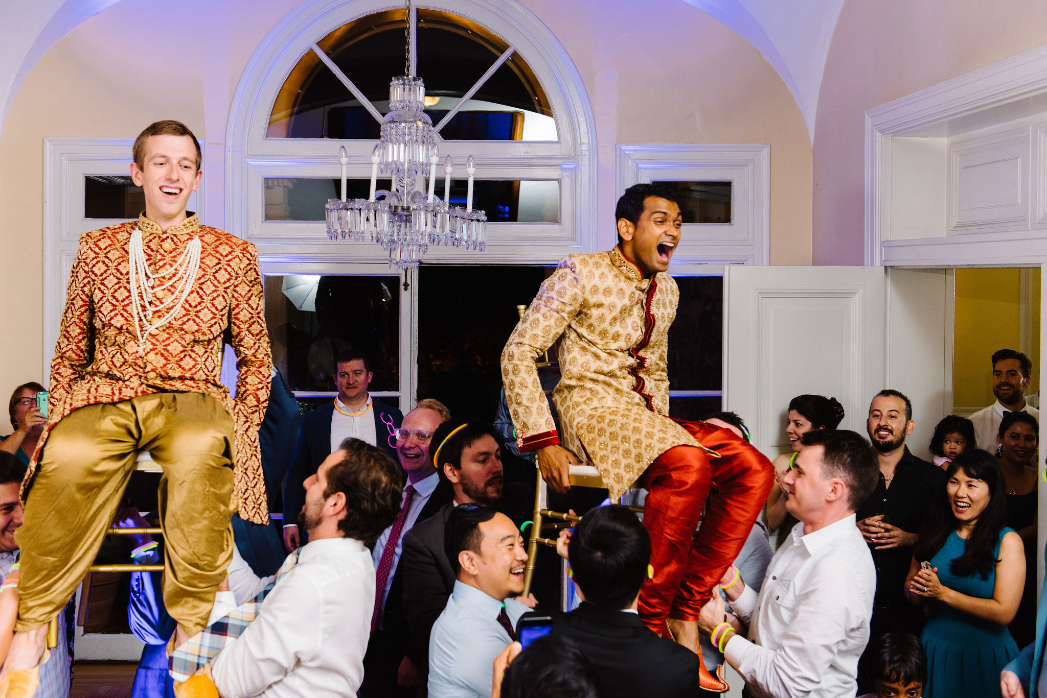 Two men are lifted up on chairs during their wedding reception