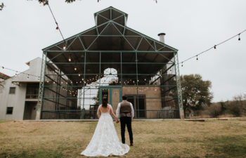 A wedding couple hold hands while standing in front of an empty building frame.
